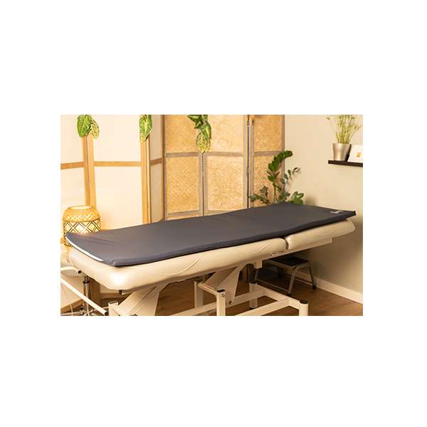 Matelas énergétique bleu Espace Mom sur table de massage ajustable, intérieur décoré avec plantes et lumière tamisée.