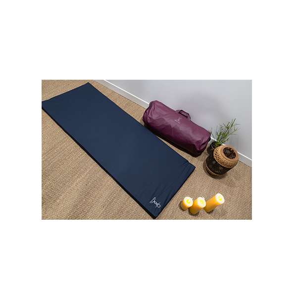 Matelas énergétique Espace Mom avec sac de transport rouge, bougies et plante sur tapis en fibres naturelles.