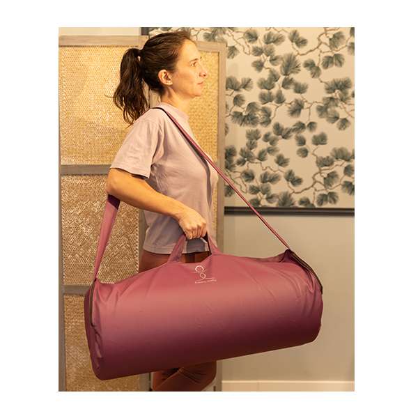 Femme tenant un sac de transport rouge pour matelas énergétique, fond décoré avec motifs végétaux.